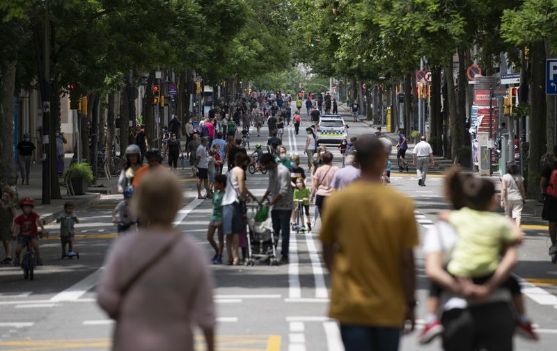 A police car patrols among people walking on a road turned into a pedestrian street on weekends in Barcelona on May 24, 2020 as the country slowly loosens a strict coronavirus lockdown. (Photo by Josep LAGO / AFP)