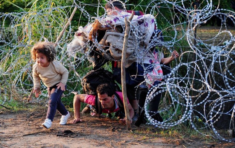 A migrant's family creeps under a barbed fence near the village of Roszke, at the Hungarian-Serbian border on August 27, 2015. As Hungary scrambles to ramp up defences on its border with Serbia, refugees continued to surge into the country in record numbers, police figures confirmed. AFP PHOTO / CSABA SEGESVARI