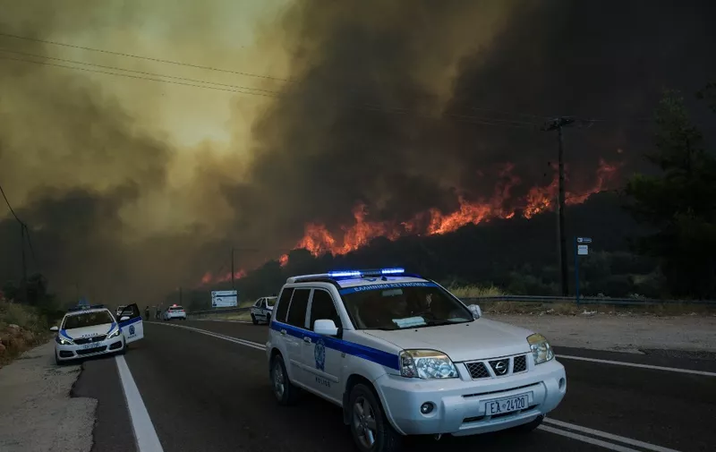 Police officers evacuate people from the area as a wildfire burns, in the village of Agios Charalabos, near Athens, on July 18, 2023. Europe braced for new high temperatures on July 18, 2023, under a relentless heatwave and wildfires that have scorched swathes of the Northern Hemisphere, forcing the evacuation of 1,200 children close to a Greek seaside resort. Health authorities have sounded alarms from North America to Europe and Asia, urging people to stay hydrated and shelter from the burning sun, in a stark reminder of the effects of global warming. (Photo by Aris MESSINIS / AFP)
