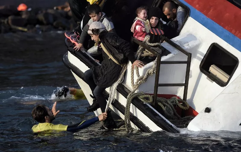Refugees and migrants try to leave their boat as it sinks off the Greek island of Lesbos island while crossing the Aegean sea from Turkey on October 30, 2015. AFP PHOTO / ARIS MESSINIS
