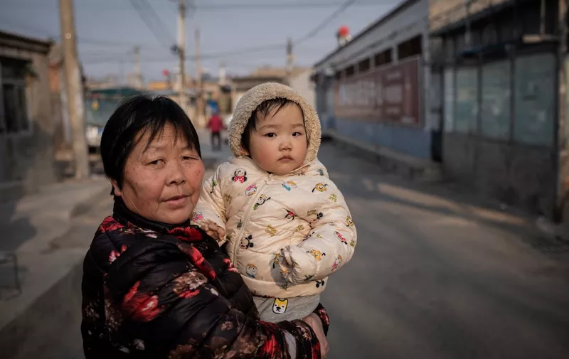 A woman holds a baby on a street in Beijing on February 25, 2021. (Photo by NICOLAS ASFOURI / AFP)