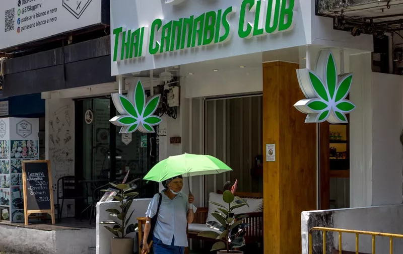 A woman sheltering from the sun under an umbrella walks past a cannabis dispensary during heatwave conditions in Bangkok on April 20, 2023. Sweltering under a blistering sun, people across South and Southeast Asia have been taking cover beneath any shelter they can find as they pray for cooling rains with record temperatures hitting the region. (Photo by Jack TAYLOR / AFP)