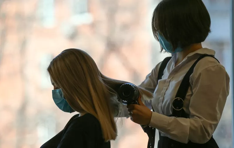 A hairdresser wearing a face mask does a woman's hair  at a barber shop in Vladivostok  on April 12, 2020, amid the COVID-19 pandemic, caused by the novel coronavirus. (Photo by Pavel Korolyov / AFP)