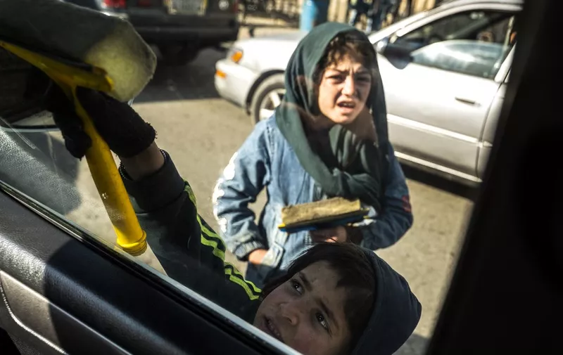 Afghan children clean a window of a car as they seek alms in return, along a road in Kabul on November 24, 2022. (Photo by Wakil KOHSAR / AFP)
