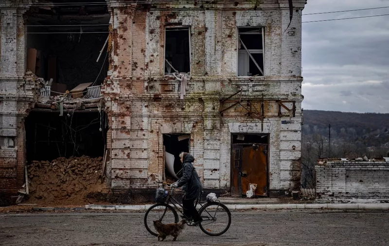 A woman rides a bicycle past a damaged building in the town of Kupiansk on November 3, 2022, Kharkiv region, amid the Russian invasion of Ukraine. (Photo by Dimitar DILKOFF / AFP)