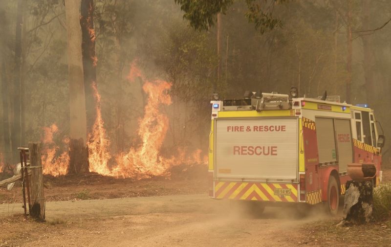 A fire engine drives past the flames as the fire front approaches homes at Nabiac, some 350kms north of Sydney, on November 15, 2019. - The death toll from devastating bushfires in eastern Australia has risen to four after a man's body was discovered in a scorched area of bushland, police said on November 14. (Photo by WILLIAM WEST / AFP)