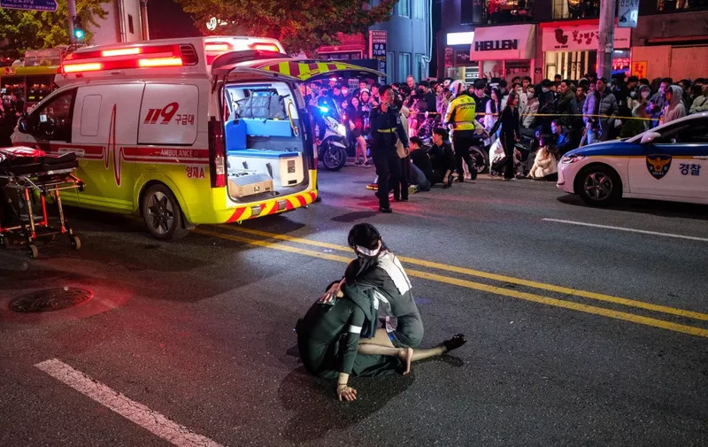 This picture taken on October 29, 2022 shows a woman comforting another as they watch proceedings after a Halloween stampede in the district of Itaewon in Seoul. - More than 150 people have been killed in a stampede at a Halloween event in Seoul, officials said on October 30, with South Korea's president vowing a thorough investigation into one of the country's worst-ever disasters. (Photo by Albert RETIEF / AFP)