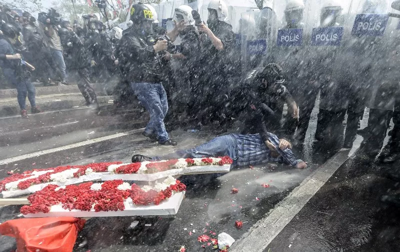 A man lies on the ground in front of a row of riot police as Turkish police use a water cannon to disperse protestors during a May Day rally near Taksim Square in Istanbul on May 1, 2015. Turkish police on used tear gas and water cannon to disperse protesters marking May Day in the Besiktas district of Istanbul as they tried to move towards the Taksim Square protest hub of Istanbul.  AFP PHOTO / BULENT KILIC