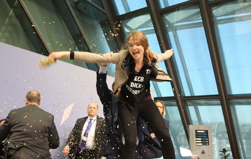 A woman jumped on the table throws papers and confetti as she interrupts a press conference by Mario Draghi, President of the European Central Bank (ECB) following a meeting of the Governing Council in Frankfurt / Main, Germany, on April 15, 2015. AFP PHOTO / DANIEL ROLAND