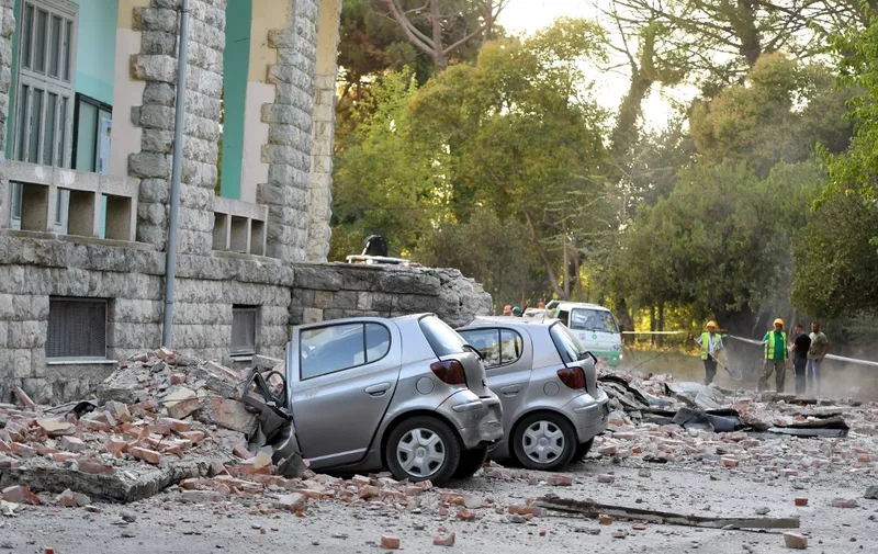 Vehicles are crushes as emergency services workers clear the ruins of a collapsed building roof in Tirana on September 21, 2019, after two earthquakes over 5.0 magnitude struck the coastline Adriatic coastline of Albania. - A strong earthquake hit Albania, forcing residents into the street in several cities, triggering power cuts in the capital and the collapse of some buildings in a nearby village. (Photo by Gent SHKULLAKU / AFP)