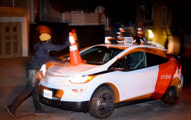 Members of SafeStreetRebel, a group of anonymous anti-car activists, place a cone on a self-driving robotaxi to disable it in San Francisco, California on July 11, 2023. Members of SafeStreetRebel, a group of anonymous anti-car activists, have been actively calling for participants to help protest the spread of robotaxis for malfunctioning and blocking traffic. (Photo by Josh Edelson / AFP)