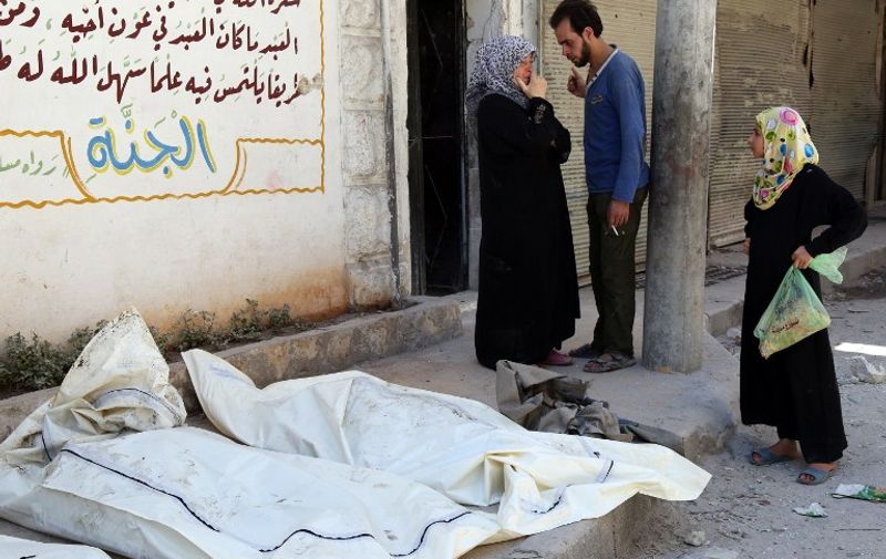 Syrians stand next to the bodies of victims following a reported attack by airstrike by government forces in the al-Kalasa neighbourhood of the northern Syrian city of Aleppo on July 19, 2015. AFP PHOTO / AMC / KHALED KHATEB
