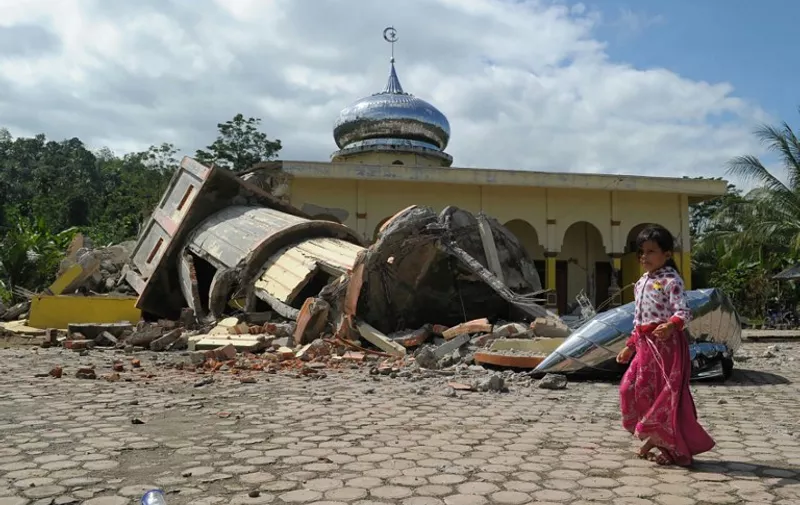 An Acehnese girl walks past a collapsed mosque minater following an earthquake in Pidie, Aceh province on December 7, 2016. 
At least 25 people died and hundreds were injured after a strong earthquake struck off Aceh province on Indonesia's Sumatra island on December 7, local officials said. / AFP PHOTO / CHAIDEER MAHYUDDIN