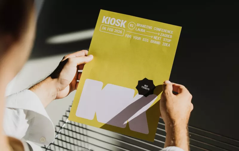 Osoba drži žutu brošuru za KIOSK konferenciju o brendiranju održanu 6. veljače 2025. u Zagrebu s crnom značkom.