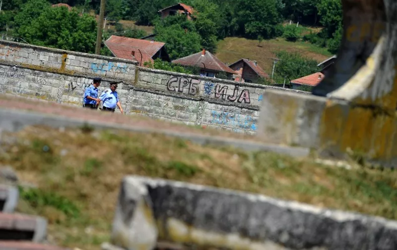 Bosnian Serb police officers walk past a Cyrillic graffito reading "Serbia" in Bratunac, near Srebrenica, on July 11, 2012. Bosnians on Wednesday buried 520 victims of the 1995 Srebrenica massacre, with the two alleged masterminds of the slaughter finally on trial for genocide. About 30,000 people were gathered at a special memorial centre in Potocari, just outside Srebrenica, for the mass funeral on the 17th anniversary of the worst atrocity on European soil since World War II.  AFP PHOTO / ANDREJ ISAKOVIC