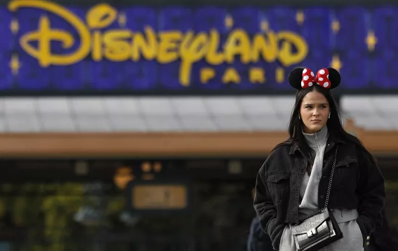 A visitor wearing Minnie Mouse ears stands near the entrance of Disneyland Paris, in Marne-la-Vallee, east of Paris, on October 16, 2023. The Walt Disney Company celebrates its 100th anniversary on October 16, marking the occasion with the release of a short film featuring more than 500 characters from 85 films. Disneyland Paris marked that anniversary with a parade showcasing a hundred of Disney's characters. (Photo by Ian LANGSDON / AFP)