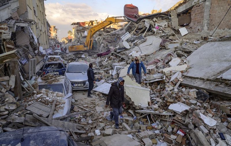 People walk across the rubble of collapsed building following two massive back-to-back earthquakes that affected both Turkey and Syria earlier in the week, in Antakiya, Hatay province, southern Turkey on February 10, 2023. - Rescuers pulled out children on February 10, 2023, from the rubble of the Turkey-Syria earthquake that struck on February 6, 2023, as the toll approached 23,000 and a winter freeze compounded the suffering for nearly one million people estimated to be in urgent need of food. (Photo by Yasin AKGUL / AFP)