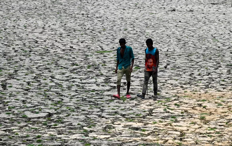 Men walk across a patch of parched riverbed of Yamuna on a hot summer day in New Delhi on June 28, 2022. (Photo by Sajjad HUSSAIN / AFP)