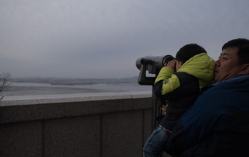 A man holds a child looking through binoculars facing North Korea at an observatory overlooking the Imjin river and Demilitarized Zone (DMZ) in Paju, on January 4, 2018. / AFP PHOTO / Ed JONES