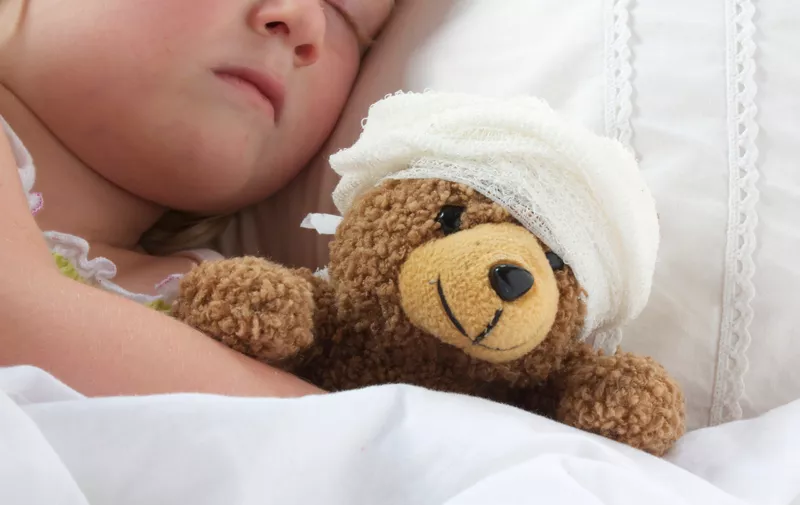 Young girl poorly in bad cuddling her teddy who also feels poorly.