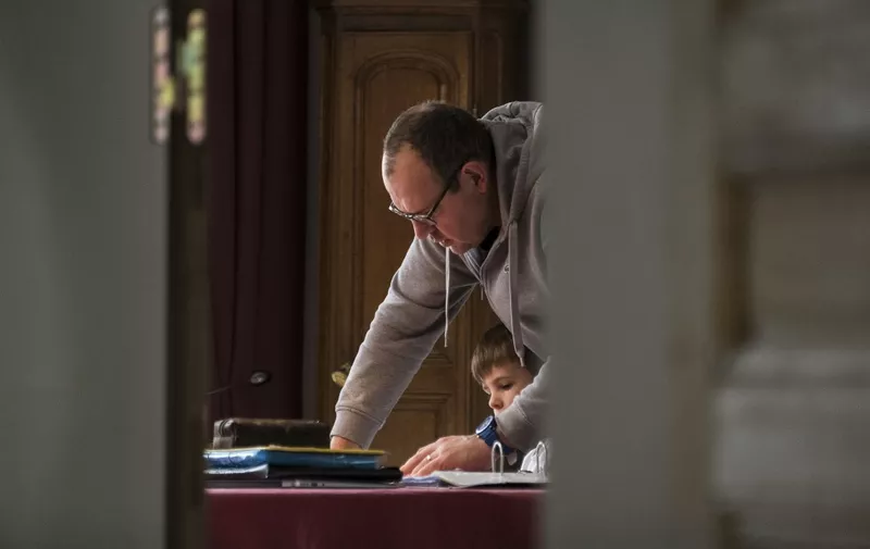 Xavier Menard helps his son, Marceau as they do the school at home on March 17, 2020, in Mulhouse, eastern France amid spread of novel coronavirus (COVID-19). - A strict lockdown requiring most people in France to remain at home came into effect at midday on March 17, 2020, prohibiting all but essential outings in a bid to curb the coronavirus spread. The country has reported 148 deaths from the virus, a number that health experts warn could soar in the coming days, seriously straining the hospital system. (Photo by SEBASTIEN BOZON / AFP)