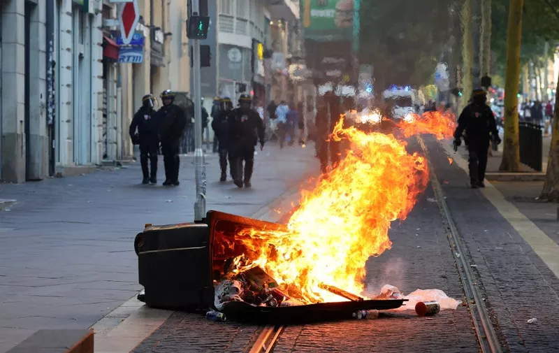 French riot police officers stand guard behind a burnt trash bin during a demonstration against police in Marseille, southern France on July 1, 2023, after a fourth consecutive night of rioting in France over the killing of a teenager by police. French police arrested 1311 people nationwide during a fourth consecutive night of rioting over the killing of a teenager by police, the interior ministry said on July 1, 2023. France had deployed 45,000 officers overnight backed by light armoured vehicles and crack police units to quell the violence over the death of 17-year-old Nahel, killed during a traffic stop in a Paris suburb on June 27, 2023. (Photo by CLEMENT MAHOUDEAU / AFP)