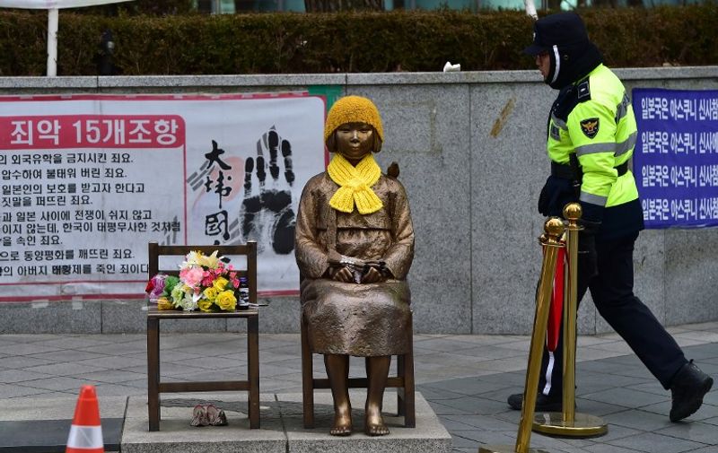A South Korean policeman walks past a statue (C) of a teenage girl in traditional costume called the "peace monument" for former "comfort women" who served as sex slaves for Japanese soldiers during World War II, in front of the Japanese embassy  in Seoul on December 29, 2015.  South Korean officials met with former "comfort women" to seek their support for a landmark deal with Japan, after criticism it does not properly atone for the treatment of women forced into WWII army brothels.  AFP PHOTO / JUNG YEON-JE / AFP PHOTO / JUNG YEON-JE