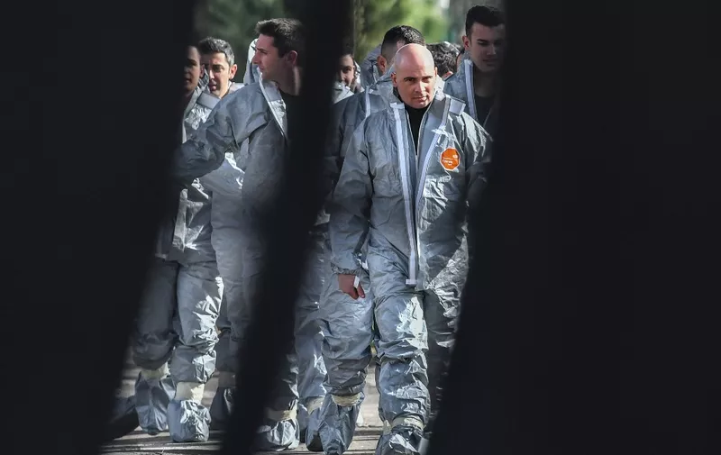 A picture taken through the entrance of the Cecchignola military quarantine center, south of Rome, on February 3, 2020 shows military personnel in protective suits walking across the center where Italian citizens repatriated from the coronavirus hot-zone of Wuhan are to be placed in quarantine after landing earlier at the nearby military airport of Pratica di Mare. (Photo by Tiziana FABI / AFP)