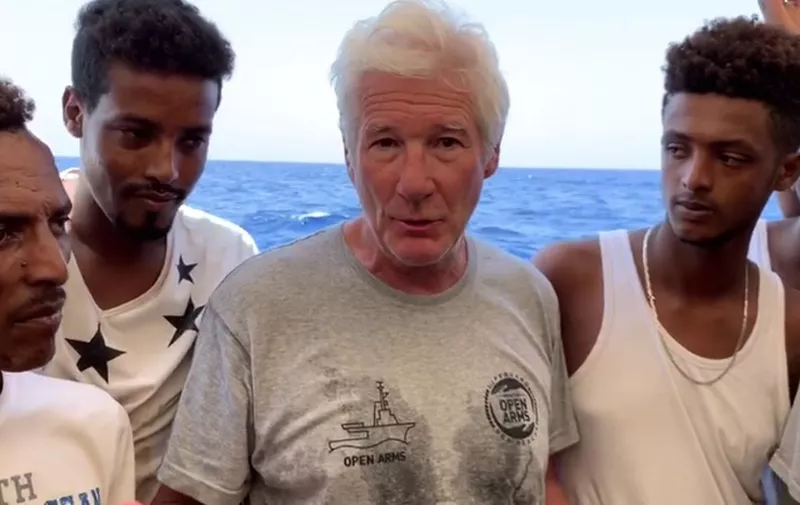 An image grab taken from a video released by the Spanish NGO Proactiva Open Arms on August 9, 2019 shows US actor Richard Gere (C) speaking on board the charity's boat transporting 121 migrants rescued from the middle of the Mediterranean Sea and waiting for a port to dock at. (Photo by HO / PROACTIVA OPEN ARMS / AFP) / RESTRICTED TO EDITORIAL USE - MANDATORY CREDIT "AFP PHOTO / PROACTIVA OPEN ARMS" - NO MARKETING - NO ADVERTISING CAMPAIGNS - DISTRIBUTED AS A SERVICE TO CLIENTS - NO RESALE