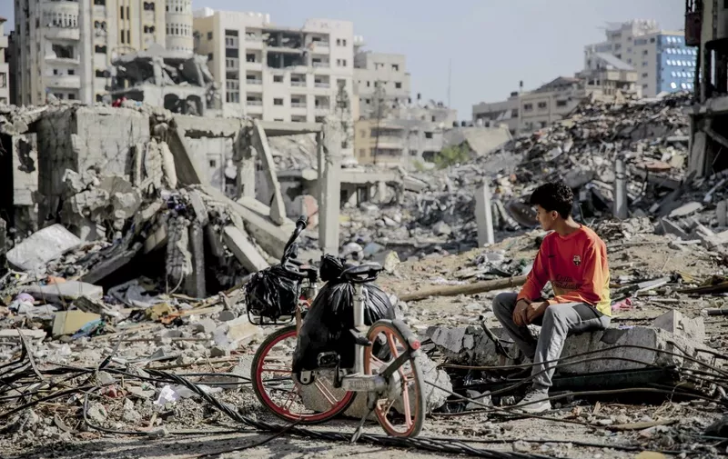 A Palestinian youth sits next to his bicycle amid the rubble of destroyed buildings in Gaza City on the northern Gaza strip following weeks of Israeli bombardment, as a four-day ceasefire took effect on November 24, 2023. The truce in the Israel-Hamas war began on November 24 and appeared to be holding, under a deal that will see hostages released in exchange for Palestinian prisoners. (Photo by AFP)