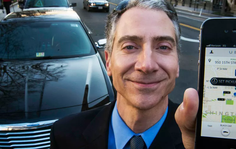 Peter Faris, CEO of Szabo Faris LLC Transportation Solutions, stands in front of one of his vehicles while holding a smart phone with an app that orders up his sedan service  February 14, 2013 in Washington, DC. Faris, an independent driver who works with Uber, a technology firm which has created a mobile app which allows consumers to use their device to request a nearby taxi or limousine. Uber is among a number of apps which are being deployed in cities in the United States and worldwide.     AFP Photo/Paul J. Richards        (Photo credit should read PAUL J. RICHARDS/AFP/Getty Images)