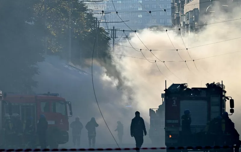 Smoke rises over the street as Ukrainian firefighters prepares, after a drone attack in Kyiv on October 17, 2022, amid the Russian invasion of Ukraine. - Ukraine officials said on October 17, 2022 that the capital Kyiv had been struck four times in an early morning Russian attack with Iranian drones that damaged a residential building and targeted the central train station. (Photo by Sergei SUPINSKY / AFP)