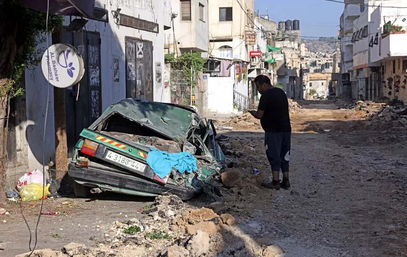A man stands next to a wrecked car after an Israeli military operation in the Jenin refugee camp, occupied West Bank, on July 4, 2023. Israeli forces killed nine Palestinians in a large-scale operation Monday in the occupied West Bank that the army labelled an "extensive counterterrorism effort," involving air strikes and hundreds of troops. (Photo by RONALDO SCHEMIDT / AFP)