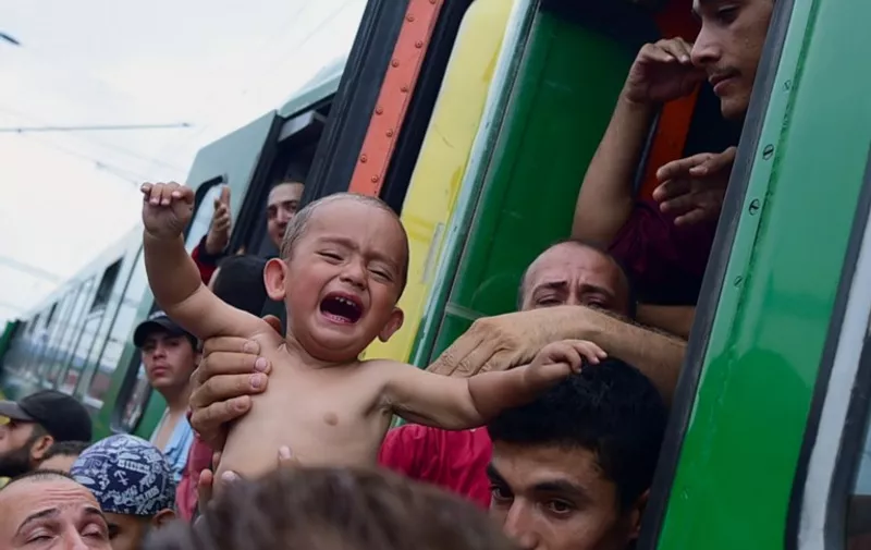 A migrant holds a crying boy out of a local train coming from Budapest and heading to the Austrian border, that has been stopped in Bicske, west of the Hungarian capital on September 3, 2015. The train carrying between 200 and 300 migrants left Budapest's main international train station after authorities re-opened the station to migrants as the EU is grappling with an unprecedented influx of people fleeing war, repression and poverty in what the bloc has described as its worst refugee crisis in 50 years.  
AFP PHOTO / ATTILA KISBENEDEK