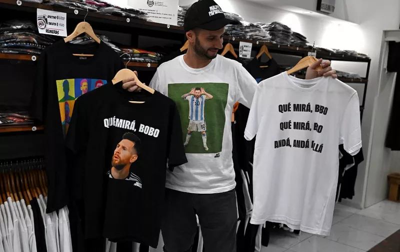 A man holds t-shirts with an image of Argentine forward Lionel Messi and a phrase reading "What are you looking at, you fool?" at a store in Buenos Aires, on December 12, 2022. - Argentine fans' pride at finally seeing Lionel Messi in charismatic leader mode sparked a commercial furore by selling products with a quarrelsome phrase of his after defeating the Netherlands (4-3 on penalties) in the quarterfinals of the Qatar-2022 World Cup. (Photo by Luis ROBAYO / AFP)