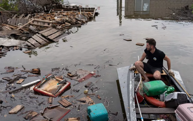 An animal rescue volunteer, moves among floating debris on a boat in floodwaters at Kherson on June 8, 2023, after the city was engulfed by rising water levels following damage sustained at Kakhovka hydroelectric power plant dam. Ukrainian President Volodymyr Zelensky has visited the region flooded by the breached Kakhovka dam, as the regional governor said 600 square kilometres were underwater. (Photo by ALEKSEY FILIPPOV / AFP)