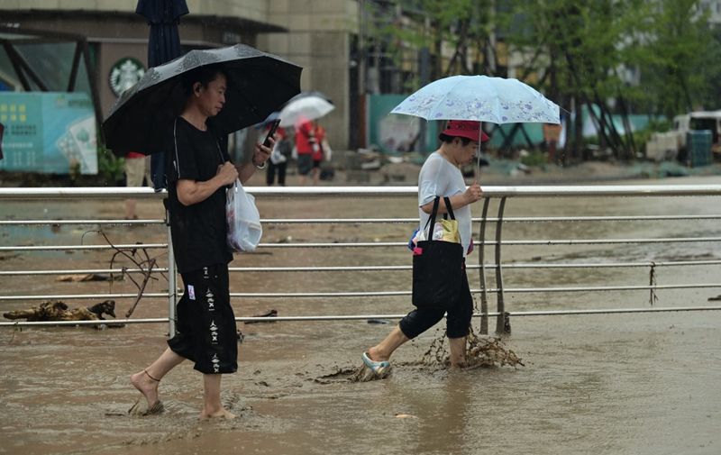 People walk along a water laden street, after heavy rains in Mentougou district in Beijing on July 31, 2023. Heavy rains battered northern China on July 31, killing at least two people in Beijing while washing away cars and inundating subway stations, with the capital issuing its highest alerts for flooding and landslides. (Photo by Pedro PARDO / AFP)