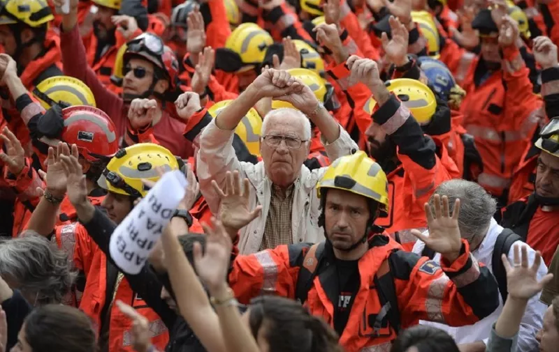 Protesters joined by firefighters raise their hands as they gather during a general strike in Barcelona called by Catalan unions on October 3, 2017.
Large numbers of Catalans are expected to observe a general strike today to condemn police violence at a banned weekend referendum on independence, as Madrid comes under growing international pressure to resolve its worst political crisis in decades. / AFP PHOTO / Josep LAGO