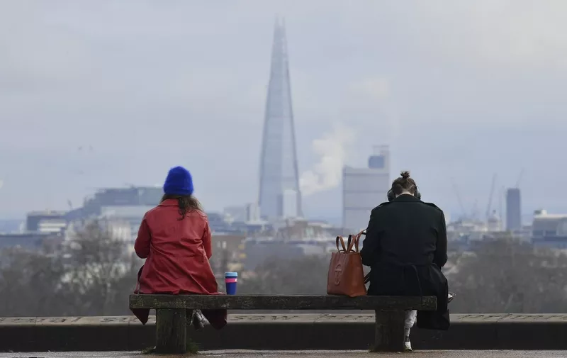 People sit at a social distance from one another on a bench on the top of Primrose Hill in London on January 12, 2021 with the Shard Tower in the background as life continues under Britain's third lockdown since the start of the coronavirus pandemic. - People who flout coronavirus lockdown rules are putting lives at risk, the British government said on Tuesday, as cases surge to record highs and rumours swirl of potentially tougher restrictions. (Photo by JUSTIN TALLIS / AFP)