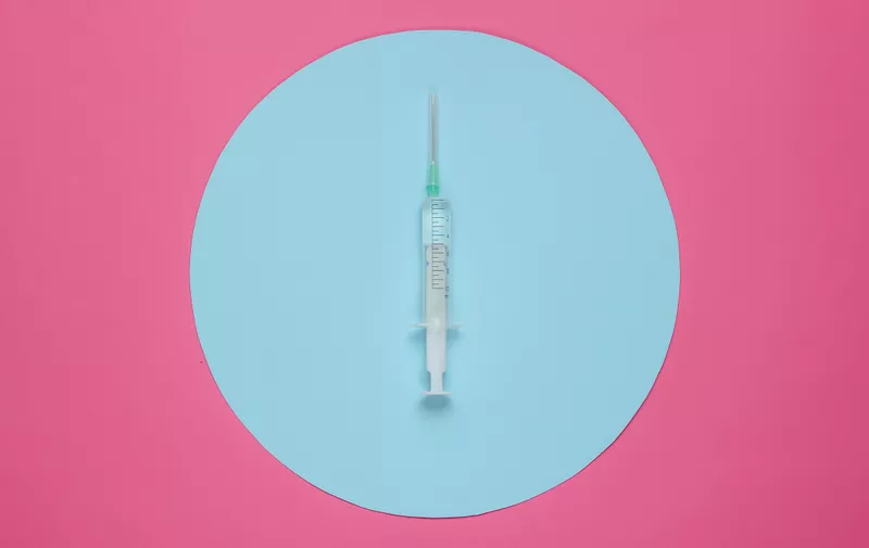 Syringe on pink background with blue circle in the center. Minimalistic medical concept.