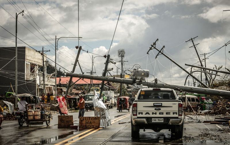 Fallen electric pylons block a road while a sign asking for food (L) is displayed along a road in Surigao City, Surigao del norte province, on December 19, 2021, days after super Typhoon Rai devastated the city. (Photo by Ferdinandh CABRERA / AFP)