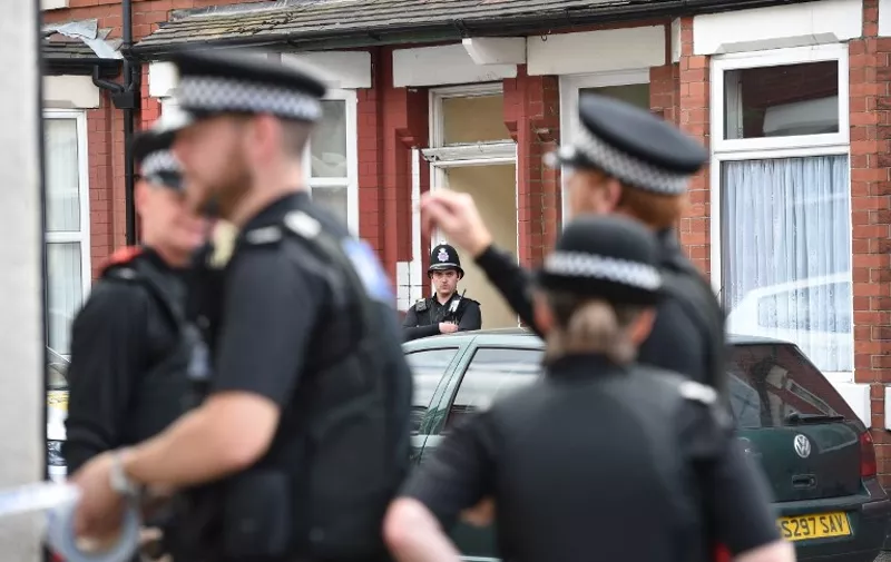 A police officer stands guard outside the door of a property in the Moss Side area of Manchester on May 27, 2017 during an operation that also involved bomb disposal units. 
British police said they arrested two more people during raids Saturday in connection with the suicide bombing at a Manchester concert, with a "large part" of the network behind the attack now being held. / AFP PHOTO / Oli SCARFF