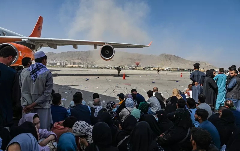 Afghan people sit as they wait to leave the Kabul airport in Kabul on August 16, 2021, after a stunningly swift end to Afghanistan's 20-year war, as thousands of people mobbed the city's airport trying to flee the group's feared hardline brand of Islamist rule. (Photo by Wakil Kohsar / AFP)