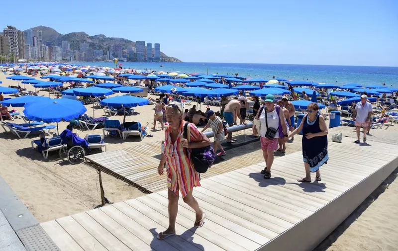 People leave as others sunbathe at Levante Beach, in Benidorm on June 7, 2022. Whether it's chefs, bar staff or dishwashers, many bars, restaurants and cafes across Benidorm are struggling to recruit workers, generating a new source of tension after two years of pandemic. (Photo by JOSE JORDAN / AFP)