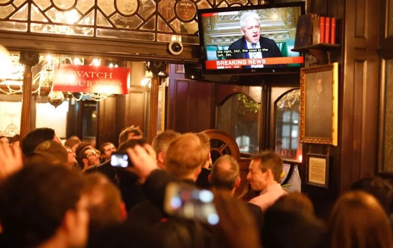 Drinkers watch a television screen in a pub in Whitehall as John Bercow, Speaker of the House declares that Prime Minister Theresa May's Brexit deal was defeated by 149 votes in an historic parliamentary vote on March 12, 2019. (Photo by Tolga AKMEN / AFP)