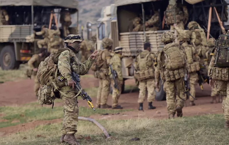 A soldier gestures as others climb a military vehicle during a simulated military excercise of the British Army Training Unit in Kenya (BATUK) together with the Kenya Defence Forces (KDF) at the ol-Daiga ranch, high on Kenyas Laikipia plateau on March 26, 2018. - Britain's 16 Air Assault Brigade was in Kenya with three companies of Gurkhas, a storied regiment made up predominately of Nepalese recruits, with their signature curved kukri knives. In recent years, infantry units were sent to Kenya for their final training before being deployed to Afghanistan and, for "rapid reaction force" 16 Air Assault, being always battle-ready is a point of pride. (Photo by TONY KARUMBA / AFP)