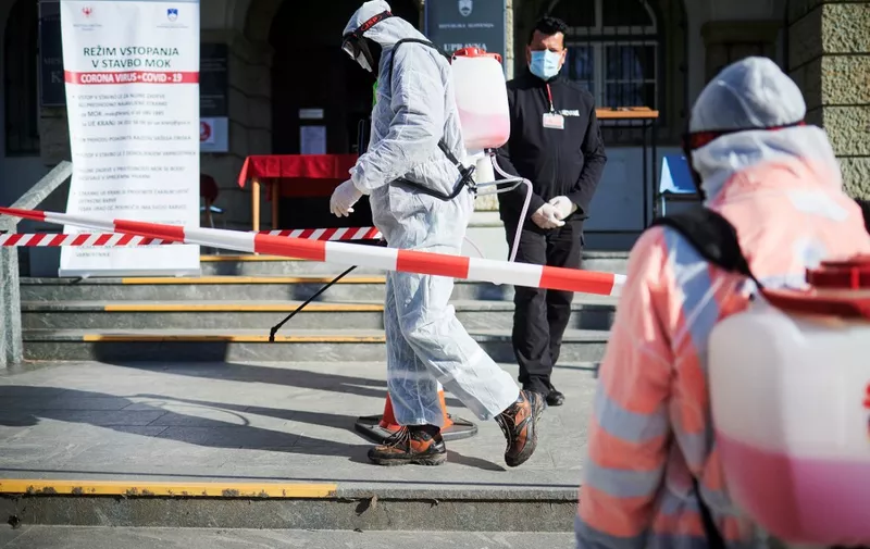 Workers wearing protective clothes disinfect entrance of the Town Hall in Kranj, Slovenia, on March 23, 2020 amid concerns over the spread of the COVID-19 coronavirus. (Photo by Jure Makovec / AFP)