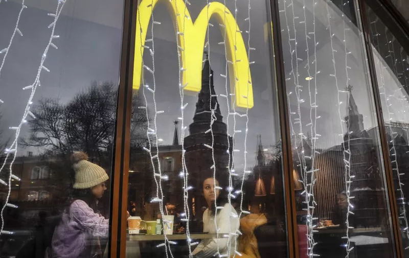 (FILES) In this file photo taken on January 30, 2020, people look out of the window of a McDonald's restaurant as the towers of the Kremlin are reflected in Moscow. - As a growing list of US multinational businesses, from Apple to Levi's, suspend activities in Russia, some companies have chosen to stay in the country despite the risks to their reputation. But following last month's invasion of Ukraine, firms such as Pepsi and McDonald's face mounting pressure: Calls for repercussions for the recalcitrant are appearing on social media under hashtags such as #BoycottMcDonalds and #BoycottPepsi. (Photo by Alexander NEMENOV / AFP)