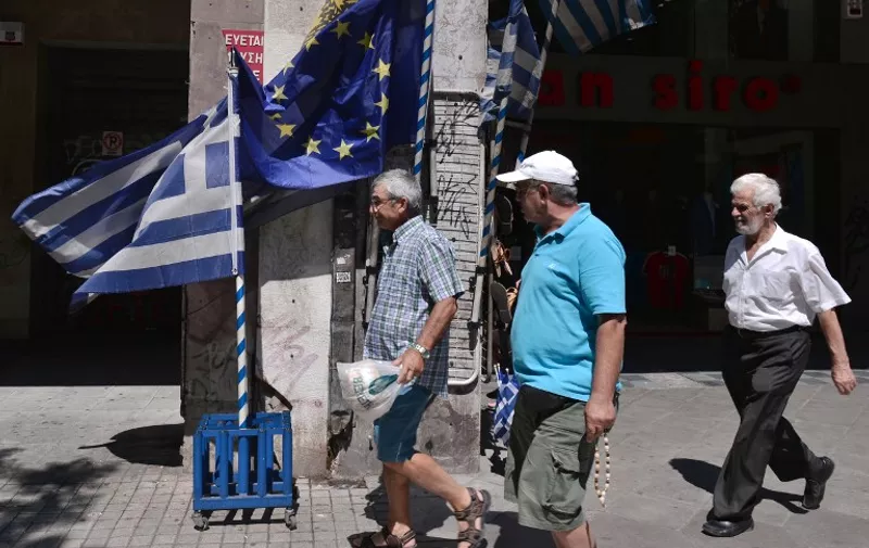 People  walk past Greek and European Union flags on sale in Athens, on July 6, 2015.  Germany said that there was currently "no basis" for talks with Greece on a new bailout package or debt relief, following a resounding 'No' in a referendum on creditors' proposals. AFP PHOTO/ LOUISA GOULIAMAKI