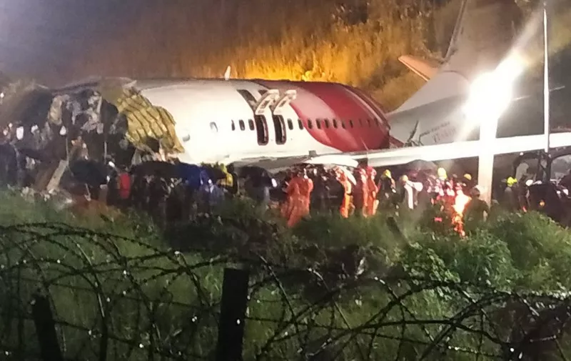 First responders gather around the wreckage of an Air India Express jet, which was carrying more than 190 passengers and crew from Dubai, after it crashed by overshooting the runway at Calicut International Airport in Karipur, Kerala, on August 7, 2020. - At least 14 people died and 15 others were critically injured when a passenger jet skidded off the runway after landing in heavy rain in India, police said on August 7. (Photo by - / AFP)